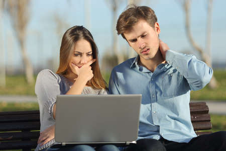 Worried students or entrepreneurs watching a laptop sitting on a bench in a park