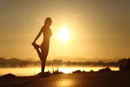 Silhouette of a fitness woman profile stretching at sunrise with the sun in the background
