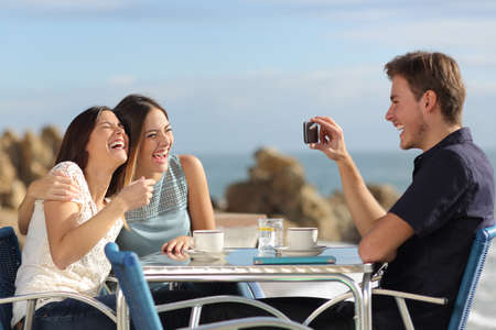 Friends on vacations laughing and taking photo with a smart phone in a restaurant on the beach