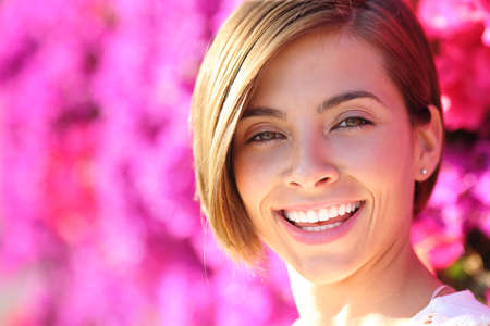 Beautiful woman smiling with white perfect teeth with a warmth lot of pink flowers in the backgroundの写真素材