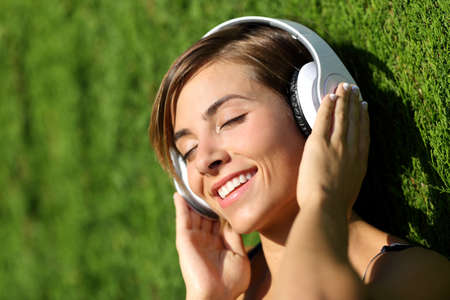 Happy girl listening to the music with headphones in a park with a green blurred backgroundの写真素材