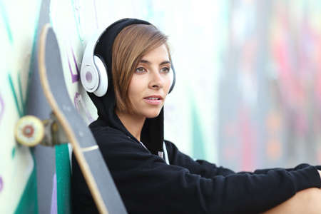 Young skater girl listening to the music with headphones with a blurred graffiti wall in the backgroundの写真素材
