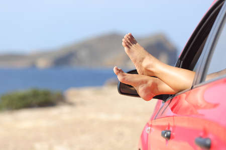 Woman feet relaxing in a car on the beach with the sea in the backgroundの写真素材