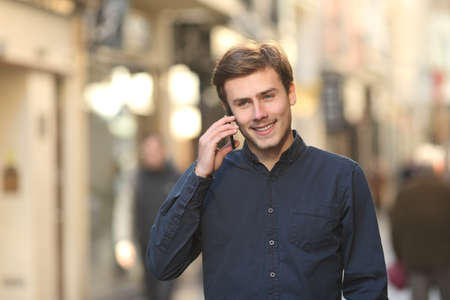 Front view of a happy man calling on the phone walking on the streetの写真素材