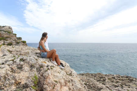 Teenager couple hugging and looking at horizon on a cliffの写真素材