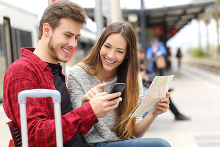 Tourists travelers consulting gps and guide from a smart phone in a train station Tourists travelers consulting gps and guide from a smart phone in a train station