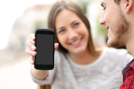 Happy couple showing apps in a blank smart phone screen outdoors