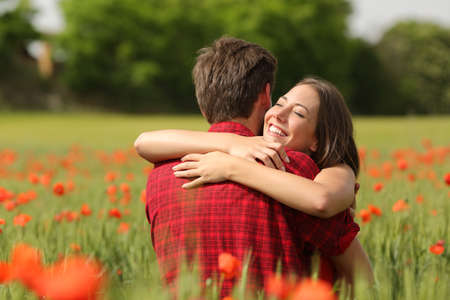 Happy couple hugging affectionate after proposal in a green field with red flowersの写真素材