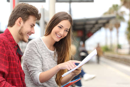 Happy couple of students studying and learning in a train stationの写真素材