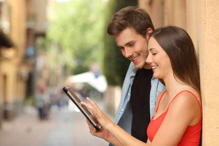 Profile of a happy couple browsing a tablet in the streetの写真素材