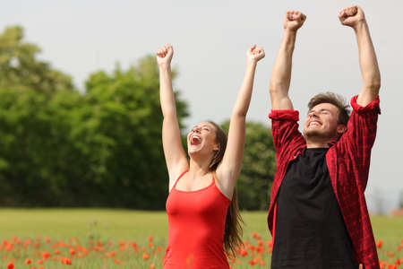 Euphoric happy couple raising arms in a country field with red flowersの写真素材