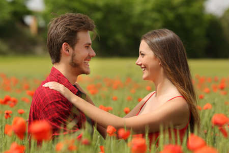 Happy couple looking each other affectionate in a field with red poppy flowersの写真素材