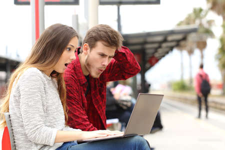 Couple worried and surprised watching a laptop in a train station while they are waiting