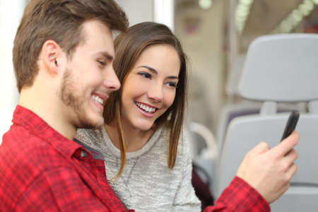 Couple of happy passengers sharing a smart phone traveling inside a trainの写真素材