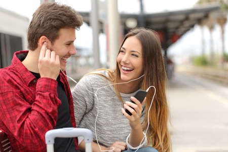 Happy couple of travelers sharing music on holidays during a travel in a train stationの写真素材