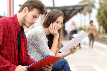 Two students studying concentrated while they are waiting transport in a train stationの写真素材