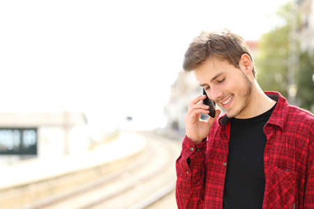 Traveler teen guy calling on the mobile phone in a train station while he is waitingの写真素材