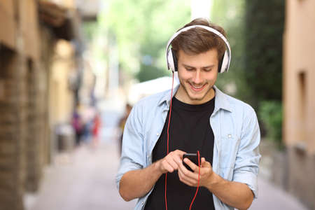 Happy guy walking and using a smart phone to listen music with headphonesの写真素材