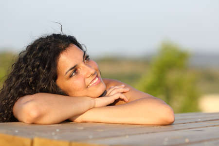 Candid girl thinking and looking sideways relaxing in a park at sunset with the sky in the backgroundの写真素材