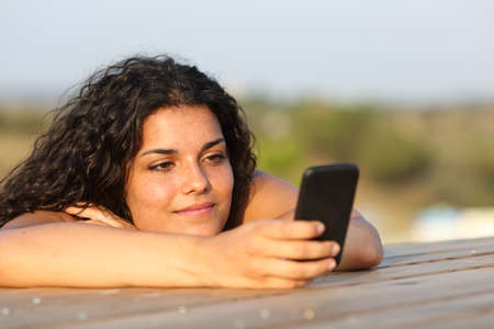 Relaxed girl watching social media in a smart phone in a park or home table with the sky in the backgroundの写真素材