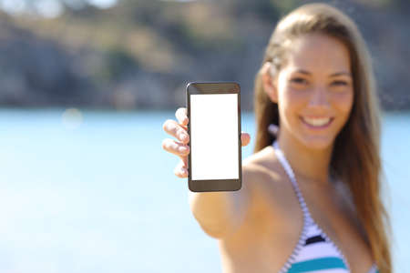 Sunbather woman wearing bikini showing blank phone screen on the beach in summer vacationsの写真素材