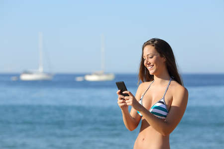 Sunbather girl wearing bikini using a smart phone on summer holidays on the beachの写真素材