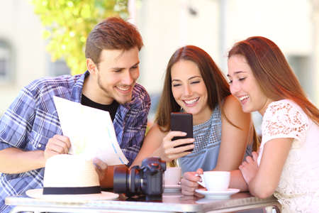 Group of three tourist friends planning vacation with a gps phone and a map in a coffee shopの写真素材