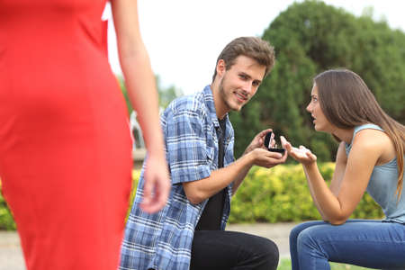 Amazed unfaithful man looking another girl during marriage proposal and his girlfriend is angryの写真素材