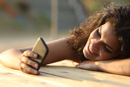 Close up portrait of a woman watching social media in a smart phone at sunset in a park tableの写真素材