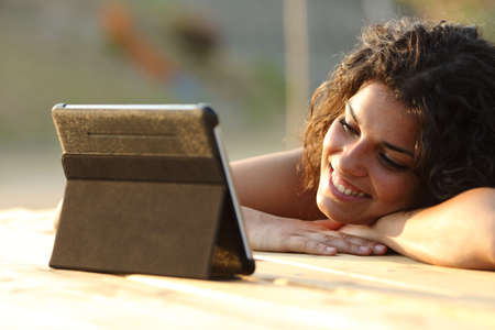 Close up of a woman watching videos on a tablet in the evening at sunset in a park tableの写真素材