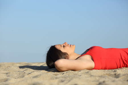 Side view of a woman resting and relaxing on the beach lying on the sand