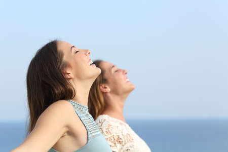 Two girls doing breath exercises inhaling fresh air on the beachの写真素材