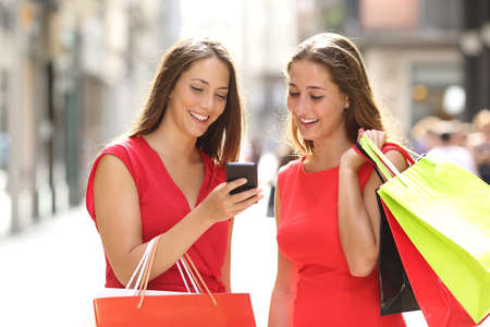 Two fashion colorful shoppers with bags shopping with a smart phone in the streetの写真素材