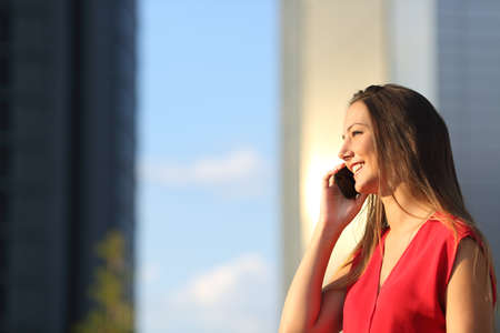 Freelancer business woman talking on the mobile phone with office buildings in the backgroundの写真素材