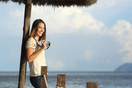 Tourist traveler girl enjoying holidays looking a seascape on the beach holding a vintage slr camera with the sea in the backgroundの写真素材