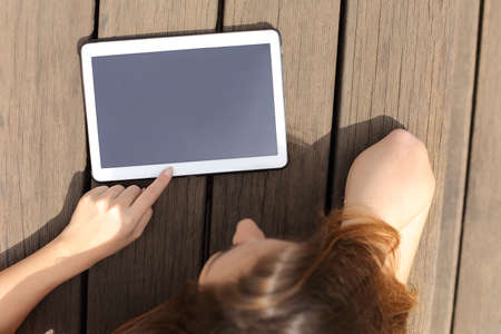 Girl using and showing a blank tablet screen lying in a bench in a sunny dayの写真素材