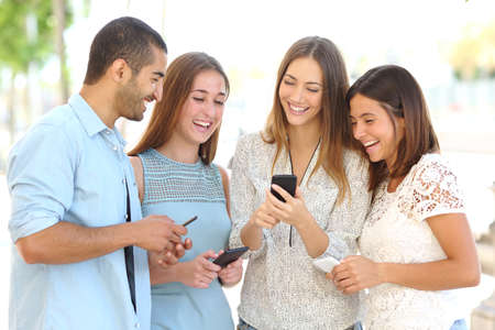 Four friends laughing happy and watching social media in a smart phone in the street every one with his own phone