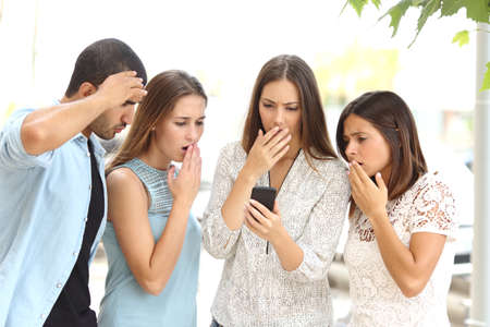 Four worried multi ethnic friends watching a smart phone in the streetの写真素材