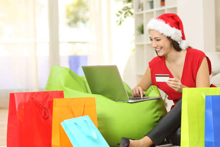 Fashion woman buying online for christmas sitting on the floor with colorful shopping bags at homeの写真素材