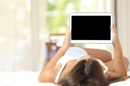 Girl lying on a bed at home using and showing a blank tablet screen