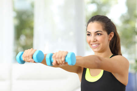 Happy fitness girl practicing sports doing weights at home