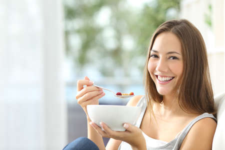 Casual happy woman dieting and eating cornflakes sitting on a couch at home Casual happy woman dieting and eating cornflakes sitting on a couch at home