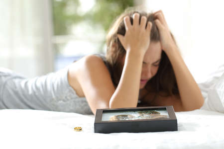 Sad wife missing her husband after divorce with a broken picture of the couple and a engagement ring in the foregroundの写真素材