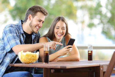 Couple sharing a smart phone sitting on a hotel or home terraceの写真素材