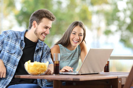Couple watching media in a laptop sitting in an hotel or home terraceの写真素材