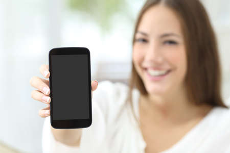 Happy housewife showing a blank smart phone screen at homeの写真素材