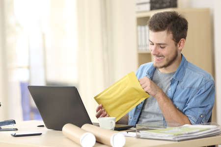 Entrepreneur opening a padded envelope in a little office or homeの写真素材