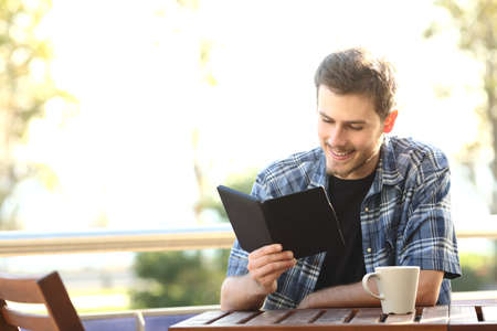 Man reading a book in an ebook reader sitting in a bar or home terrace
