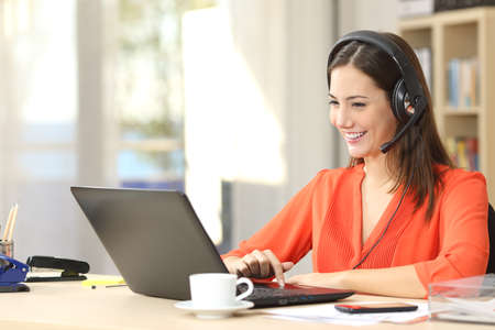 Beautiful freelancer female talking in a video conference on line with a headset with microphone and laptop in an office desktop or home deskの写真素材