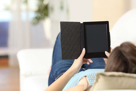 Girl reading an ebook and showing blank screen lying on a couch at homeの写真素材